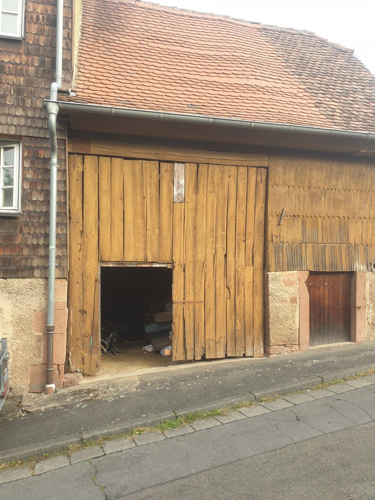 Grange ancienne avant rénovation avec porte en bois vétuste et bardage abîmé